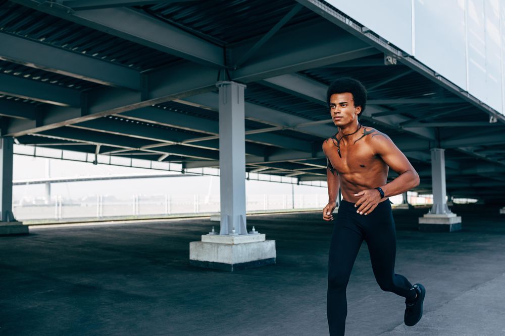 Black athletic male jogging under a bridge