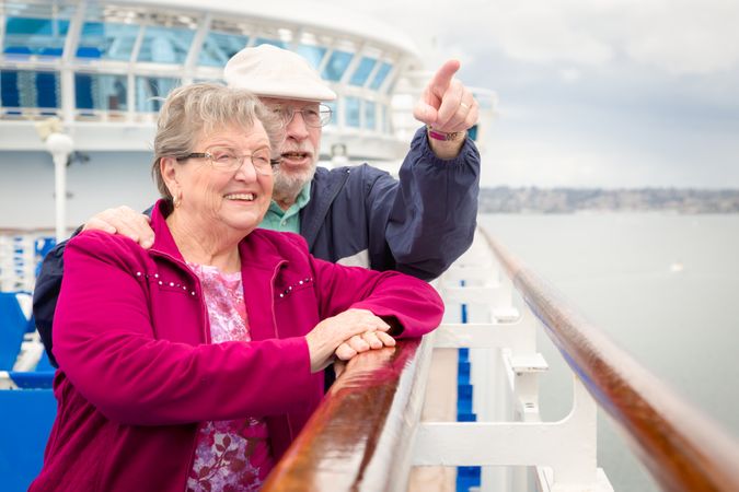 Content Older Adult Couple Enjoying The View From Their Passenger Cruise Ship Railing.