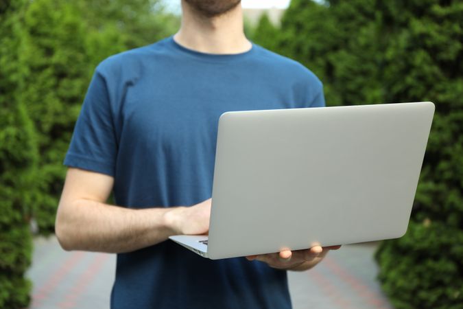 Young man in t-shirt holding laptop outdoor. Study. University