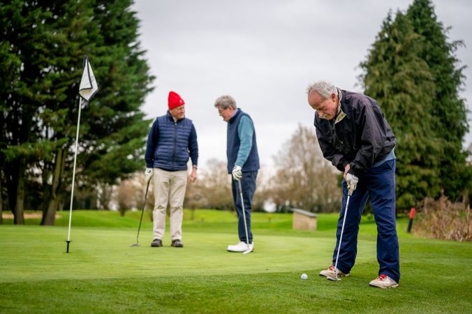 Mature male friends playing golf close to hole