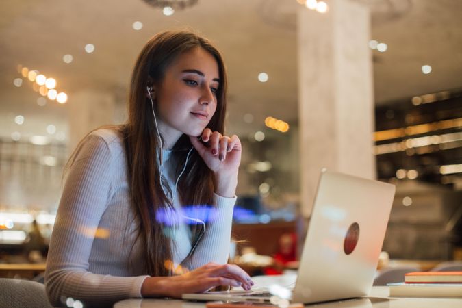 Woman in a cafe working on her laptop with earbuds