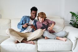 Excited Black man and white boy playing video game on sofa