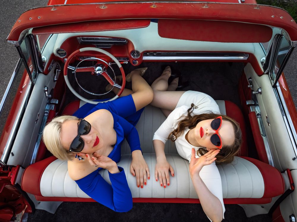 Two retro woman posing in a red convertible
