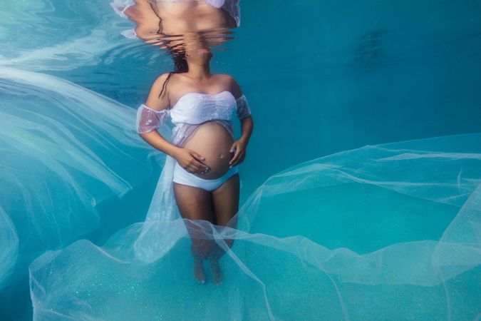 Pregnant woman in wreath and dress underwater
