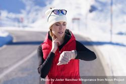 Fit woman in wintry gear checking heart rate while exercising on cold day 4jVR7R