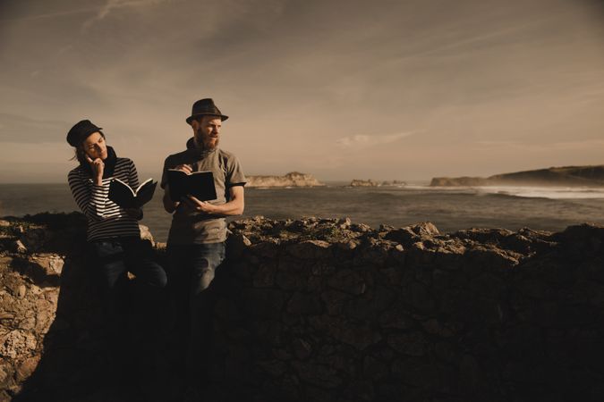 Man near woman with books near stones on shore