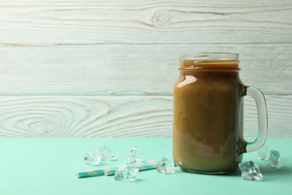 Jar of ice coffee, ice cubes and straws on mint table