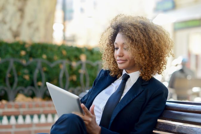 Woman in suit reading something on her digital tablet on outdoor bench