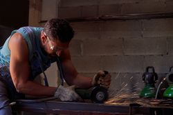 Man in protective goggles cutting metal with disk grinder