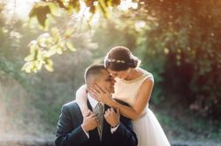 Smiling groom and bride hugging and kissing in park
