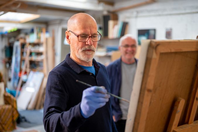Male artist painting with man looking over his shoulder