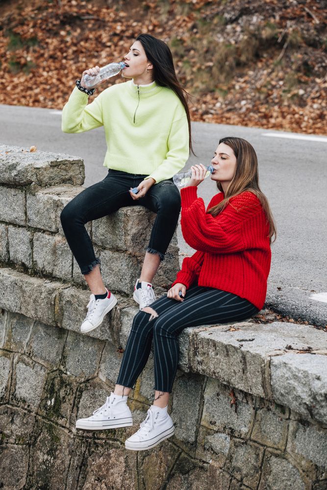 Women in sweaters drinking from bottles near road