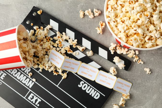 Clapperboard, tickets and buckets with popcorn on grey background, top view
