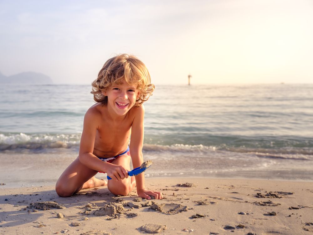 Smiling boy playing with toy shovel on sandy beach