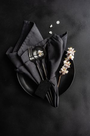 Spring floral concept with apricot blossom branch with dark plate & cutlery