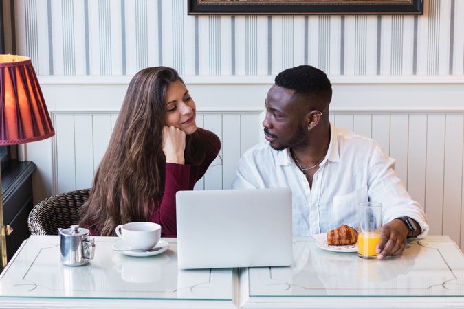 Cheerful multiethnic couple using laptop during breakfast at home