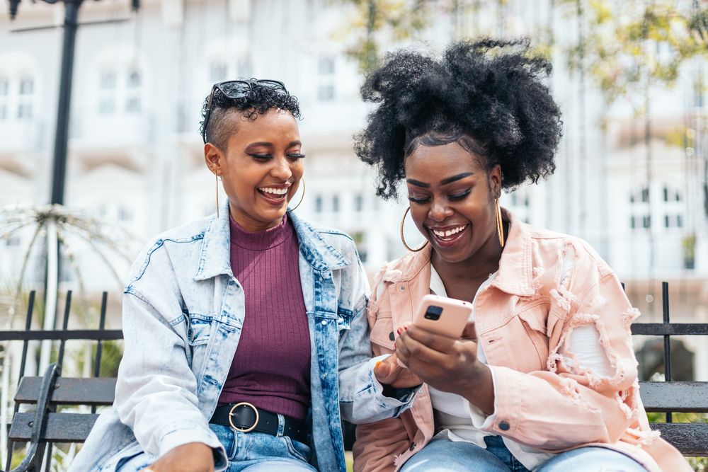 Black women friends using smartphone having fun in the city