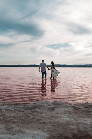 back view of adorable couple walking into an amazing beach with pink water