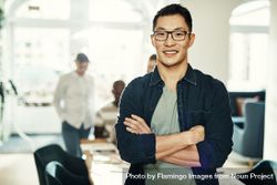 Portrait of Asian man smiling with arms crossed in bright office, landscape 4OzqL5