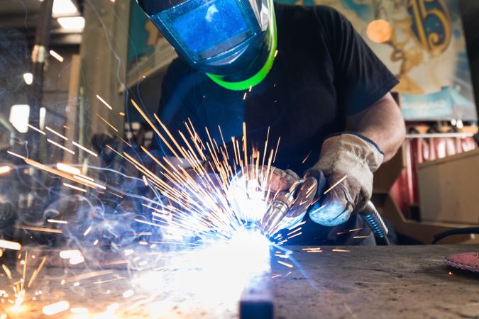 Welder in protective helmet welding metal detail in workshop