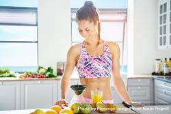 Fit woman in kitchen looking down at cutting board with juice and fresh fruit bGgeeb