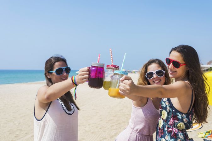 Group of smiling teenage friends toasting non alcoholic drinks on summer beach