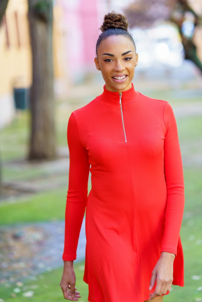 Smiling female in casual red dress strolling outside, vertical composition