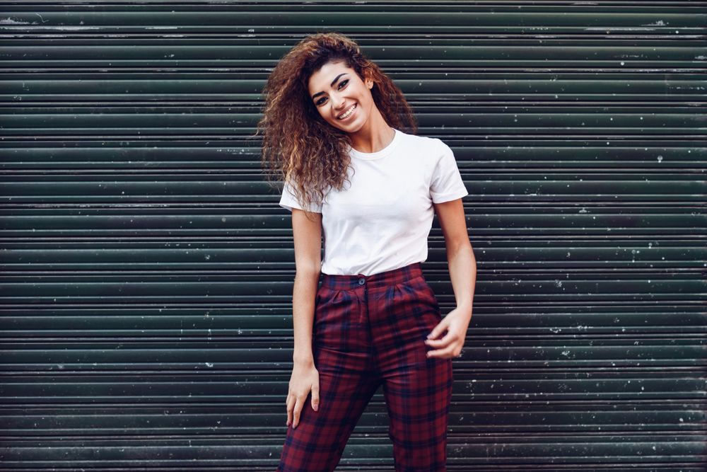 Happy Arab woman with curly hair standing outside of metal security doors