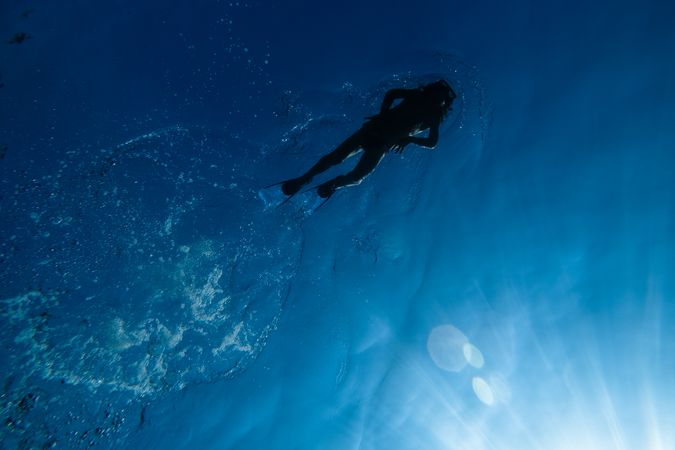 Unrecognizable diver swimming underwater in blue seawater