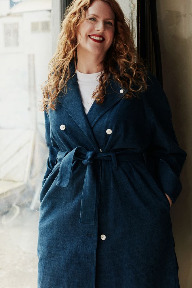 Woman in long blue coat standing in a doorway smiling
