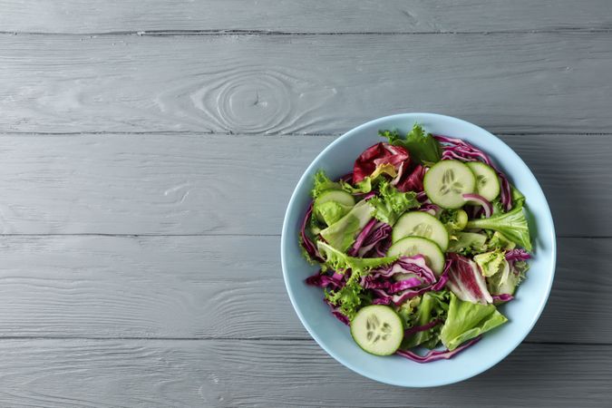 Plate with fresh salad on wooden background, space for text