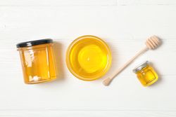 Glass jar and bowl with honey, dipper on wooden background. Flat lay