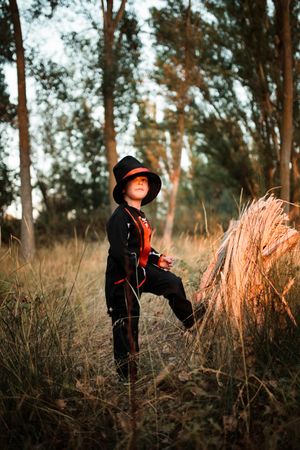 Boy in halloween costume with leg up on wood in the forest, vertical