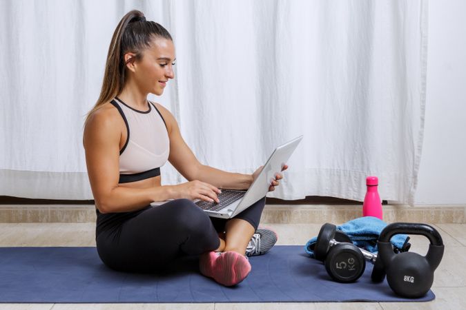 Young woman sitting on yoga mat using laptop