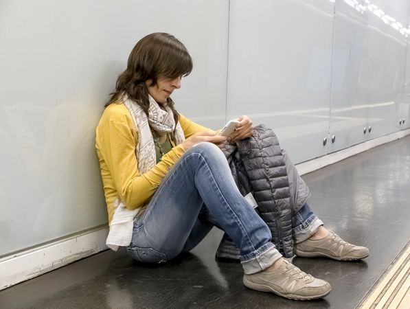 Woman sitting on ground using phone while leaning on underground platform wall