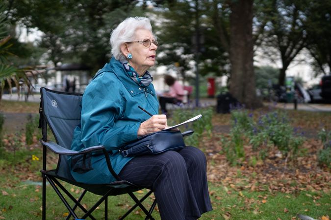 Grey haired woman sitting calmly outside drawing