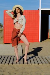 A long hair fashion model with a hat at the beach in front of a red wall