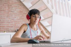 Woman working at laptop wearing red headphones 0K9YA4
