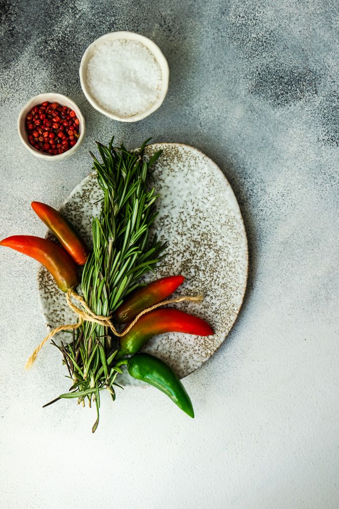 Top view of grey bowl with rosemary bunch and spicy peppers with seasoning
