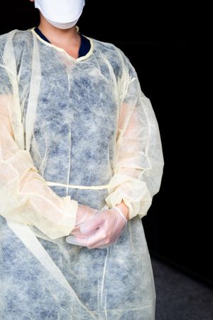 Cropped shot of nurse in disposable gown standing with hands clasped