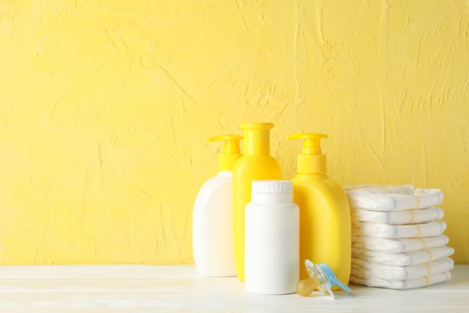 Baby hygiene accessories on wooden table against yellow background