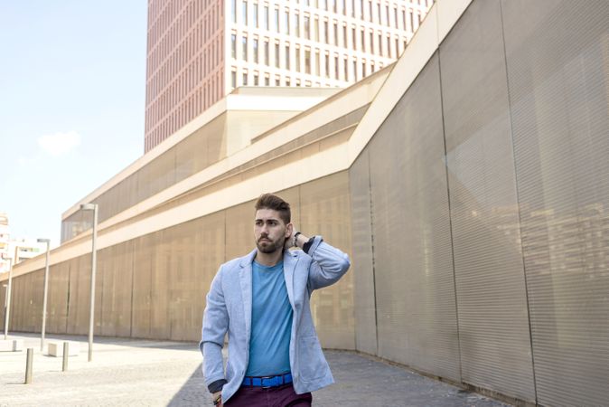 Young bearded man in front of building wearing smart casual with hand behind head