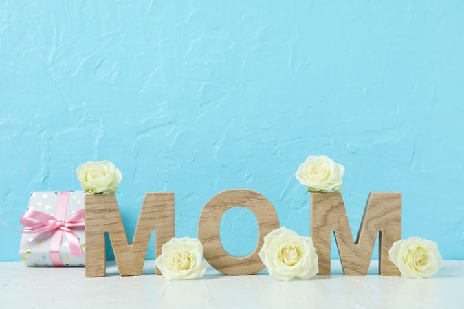 Inscription Mom with roses on pink table against color background, space for text