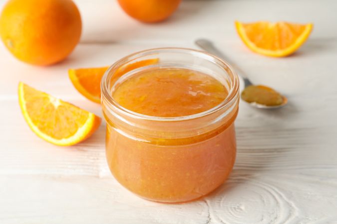 Oranges, spoon and glass jar with jam on wooden background