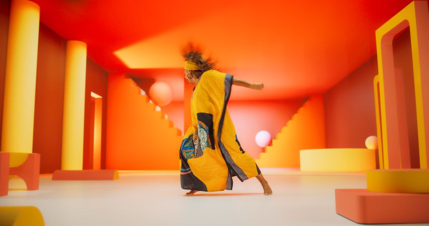 Black Woman in African Outfit Dancing Energetically in Geometric Abstract Orange Environment. Creative Female Performing Dance Choreography in Studio, Making Moves, Having Fun.