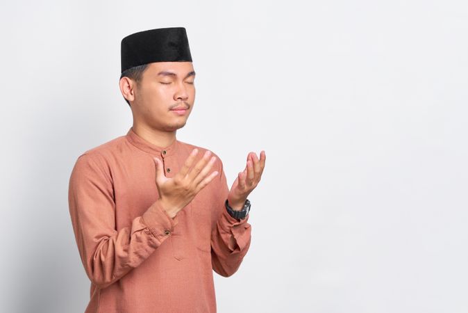 Muslim man in kufi head wear praying with his eyes closed