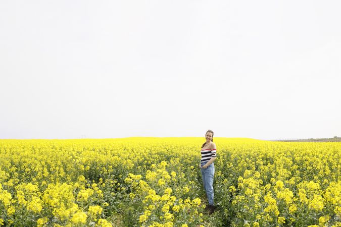 Happy woman in jeans in yellow field on overcast day