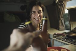 Smiling woman clanging bottles with person near cooker in camper van