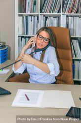Busy businesswoman talking with cell and land line phone in office 49m9gy