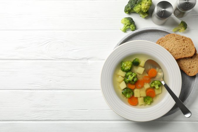 Looking down at vegetable soup on wooden table with break, copy space